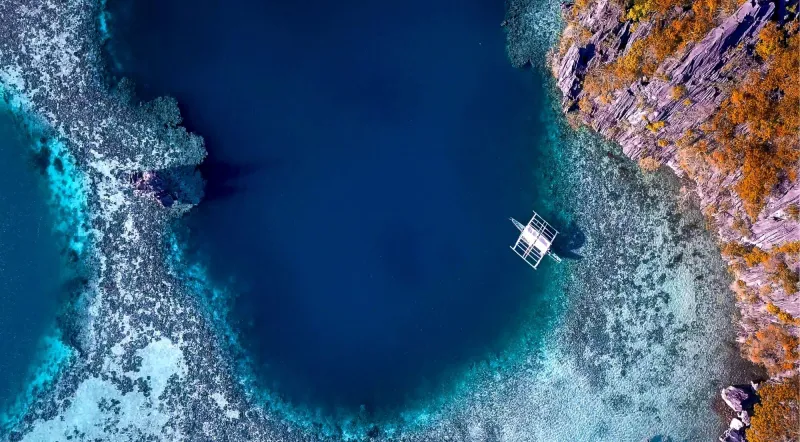 Aerial view of Barracuda Lake, Coron Island — dark deep water surrounded by orange limestone karst and shallow coral