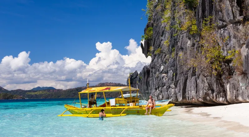 Yellow bangka boat at white-sand beach with limestone cliffs, Coron outer islands Philippines