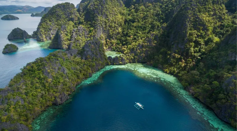 Aerial view of Coron Bay with limestone karst islands and single outrigger boat on deep blue water