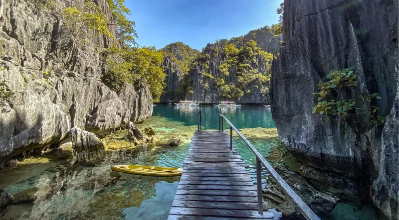 Wooden walkway at Twin Lagoon entrance with turquoise water and limestone walls, Coron Philippines